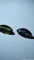 Photo showing two marquise cut sapphires, one in green color and the other displaying blue green hues, against a white textured background.