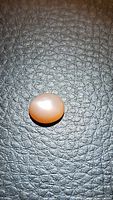 Photo of individual peach moonstone cabochon on textured dark background, showing shape, color, and surface reflective qualities.