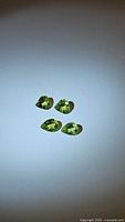 Four natural peridot gemstones placed on flat surface showing shape and color in different lighting.