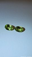 Top view of two oval cut apple green peridot gemstones placed side by side on a smooth white surface.