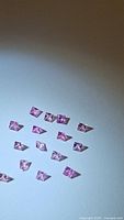 Fifteen small pink princess cut sapphires arranged on a white surface.