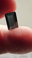 Close-up image of a rectangular emerald cut deep cobalt blue tourmaline held between fingers, showing clarity and cut.