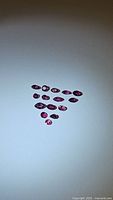 Fifteen natural untreated rubies with mixed cuts, arranged on a white surface.