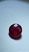 Image of a round cut deep red ruby with visible inclusions under light, showing polished surface and reflections.