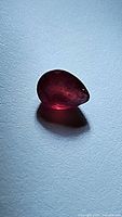Pear-shaped natural ruby gemstone placed on a white surface showing rich red color and internal inclusions.