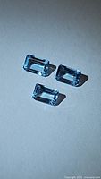 Three natural sky blue topaz gemstones with emerald cut, displayed on a flat surface with side lighting showing clarity and faceting.