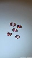 Five natural pink tourmaline gemstones of mixed cuts displayed on light surface.