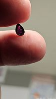 Close-up photo of pear-shaped deep purple raspberry pink sapphire held between fingers, showing stone clarity and color.