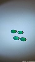 Four vivid green oval cabochon onyx gemstones displayed on white background, showing smooth polished surfaces and uniform shapes.