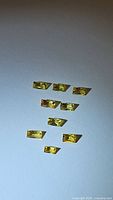Ten vivid yellow baguette cut sapphires arranged on white background, showing clarity and uniform cut.