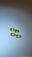 Four natural oval cut yellow sapphires displayed on white background with shadows visible. The stones appear polished and faceted, showing clarity and color consistency.