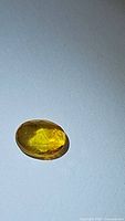 Photo of an oval shaped deep yellow fancy rose cut natural sapphire gemstone on a white surface showing the gem's color and facet pattern