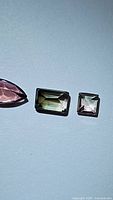 Photo showing the three tourmalines: large rectangular watermelon bicolor stone in center, smaller pink marquise to left, and smaller square bicolor to right.
