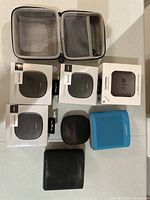 Overview of lot showing three unopened Bose SoundLink Micro boxes, open carrying case, one used SoundLink Micro and two SoundLink Color II speakers (blue and black).