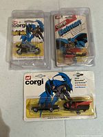 Overview of three original blister packages containing the Corgi diecast Batman motorcycle, helicopter, and Batmobile with Batboat.