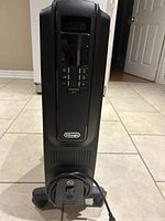 Front view of black Delonghi radiant heater showing control panel with ECO mode button and power cord neatly coiled at base.