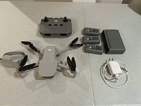Overview of DJI Mini 2 drone, controller, three batteries, charging hub, USB adapter and gimbal protector on countertop