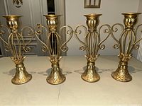 Four matching gold tone metal candlesticks arranged side by side showing front