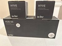 Three black boxes featuring in-lite branding: one long rectangular HUB-50 box and two smaller HYVE fixture boxes stacked on top.
