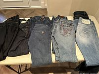 Eight pairs of ladies designer jeans in various washes and styles laid flat on table.