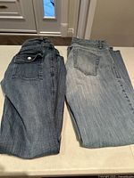 Two pairs of ladies jeans laid flat showing back pockets and overall jean condition.