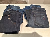 Four pairs of ladies jeans folded and displayed on a table, showing types and colors including light blue, dark blue, and black denim.