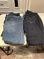 Four pairs of ladies jeans folded and stacked on a table, showing different denim colors and brands.