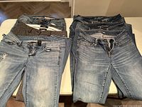 Six pairs of folded women's pants size 2 displayed on table. Includes denim and knit fabrics.