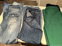 Six pairs of ladies pants size 4-5 on table including denim jeans and solid colored dress pants