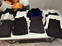 Folded assorted ladies pants arranged on a table including black, white, beige, gray, and navy colors.