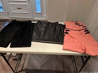 Full view of three items laid flat on table: black suede pants, black leather skirt, and coral faux suede pant suit