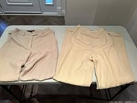 Two pairs of light beige ladies wool pants size 2 placed on a table