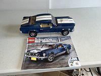 Photo of assembled blue Lego Mustang model with white racing stripes and instruction manual on table.