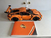 Overview of assembled orange Porsche 911 GT3 RS model with instruction manual beside it