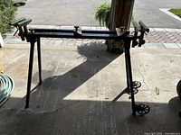 Full view of collapsible mitre saw stand in an open garage with wheels and adjustable clamps visible.