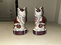 Front view of both ceramic cat figurines showing intricate detailed patterns and designs.