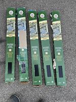 Five green cardboard boxes each labeled as containing black 3/4 inch square deck balusters for railing, placed on pavement.