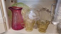 Pink textured glass pitcher, yellow sugar and creamer bowls, clear glass pitcher, decorative glass serving plates in green and clear glass