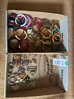 Photo showing a collection of bangles in plastic and metal, along with brooches, bracelets and a necklace laid out in cardboard boxes.