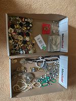 Wide view showing two boxes containing assorted costume jewellery including necklaces, rings, and clip-on earrings.