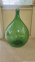 Full height view of large green glass demijohn carboy with rounded body and narrow neck.