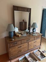 Front view of medium wood tone dresser with 7 drawers and removable mirror, two blue ceramic lamps with beige shades on top, jewelry boxes and items on dresser surface visible.