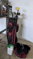 Full view of maroon and black golf bag holding all clubs, standing upright with some accessories around.