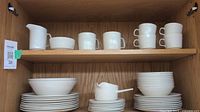 Two shelves of off-white Johnson Brothers Athena patterned dinnerware showing plates, bowls, cups, creamer, sugar, and gravy server.