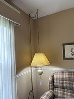 Ivory hanging ceiling lamp mounted and hanging next to a plaid armchair, with brass chain and ivory pleated shade.