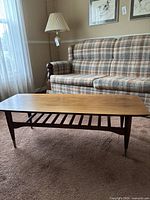 Full view of rectangular coffee table with slatted under shelf and brass-capped legs in living room setting
