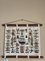 Full front view of fabric wall hanging with multiple nautical ropes, knots, and accessories mounted on white fabric with dark wood rods at top and bottom.