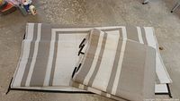 Two outdoor mats folded on top of each other showing striped pattern and material texture, some pulls visible