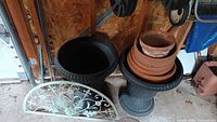 Large black plastic planters (18x22) with stacked terracotta clay pots and saucers, green decorative metal artwork on the ground