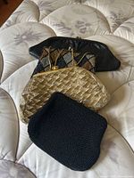 Four vintage purses arranged on a mattress including black leather, gold woven with chain strap, and two beaded bags.